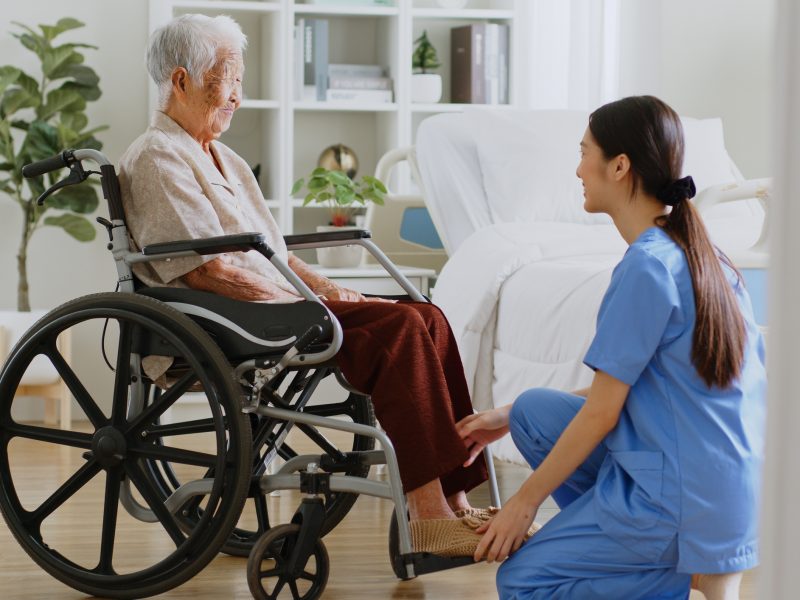 Young Asian woman, nurse, caregiver, carer help and assist a senior Asian woman on wheelchair at home